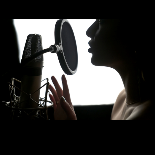 Dans cette image, il y a une silhouette d'une personne en train d'enregistrer dans un studio. Elle est de profil, face à un microphone professionnel avec un filtre anti-pop circulaire. La lumière en arrière-plan crée un effet de contraste, mettant en valeur les contours de son visage et de sa main levée, comme pour accentuer l'expression vocale. L'image évoque l'enregistrement de livres audio, de podcasts ou de voix off.