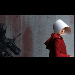 Sur un fond de mur gris texturé, une femme se tient de profil, tournée légèrement vers la caméra, vêtue d’un manteau rouge intense et coiffée d’une large coiffe blanche rigide en forme d’aile, typique des servantes dans la série La Servante écarlate (The Handmaid’s Tale). Son visage, à demi caché sous la coiffe, laisse entrevoir un regard déterminé, presque défiant, malgré l’apparente soumission imposée par sa posture et son uniforme. Sa main est posée discrètement devant elle, dans une position qui évoque à la fois l’attente, la retenue et la résignation. À l’extrême gauche de l’image, à peine visible dans l’ombre, un homme en tenue militaire noire se tient en arrière-plan, tenant une arme d’assaut en position d’alerte. Son visage est entièrement dissimulé par un casque et des lunettes tactiques, ce qui renforce son anonymat et sa fonction répressive. Il semble incarner une présence constante, silencieuse mais menaçante, renforçant le contraste entre la vulnérabilité imposée de la servante et la brutalité du régime sous-jacent. L’image est glaçante de sobriété : elle exprime, en une composition figée, la tension permanente entre contrôle armé et soumission codifiée, entre autorité invisible et résistance muette. Les couleurs sont volontairement limitées – rouge, gris, noir, blanc – pour souligner la froideur du système et l’isolement des individus dans un monde régi par la peur et la contrainte.